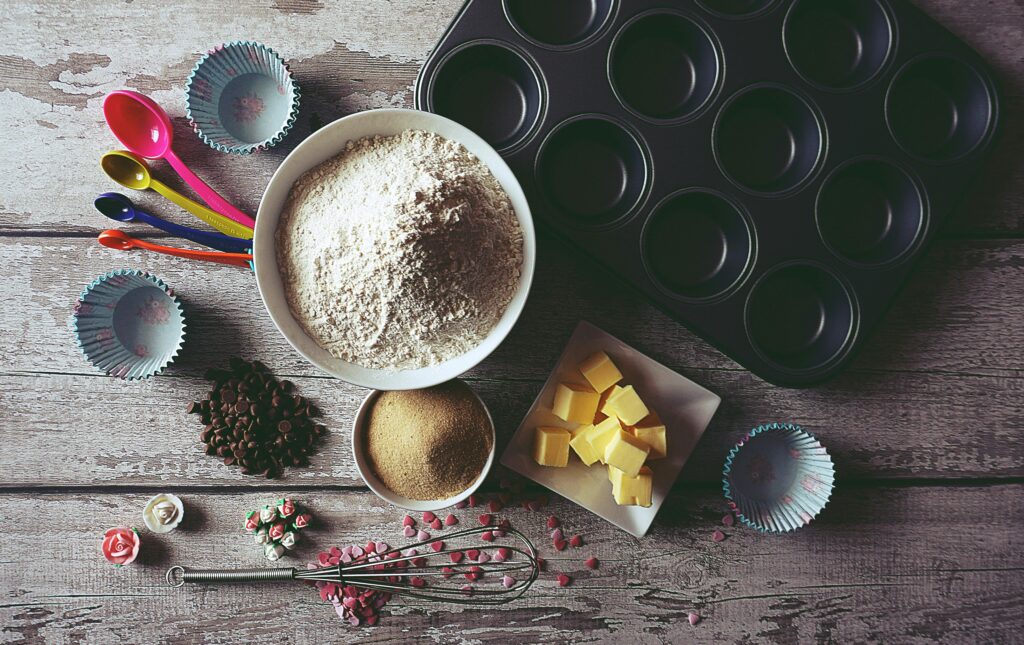 Flat lay of baking ingredients and tools for making cupcakes, including flour, butter, and chocolate chips.